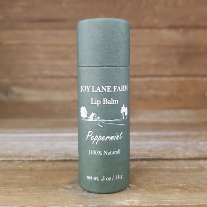 Lip balm container with 'Joy Lane Farm' branding on a wooden background