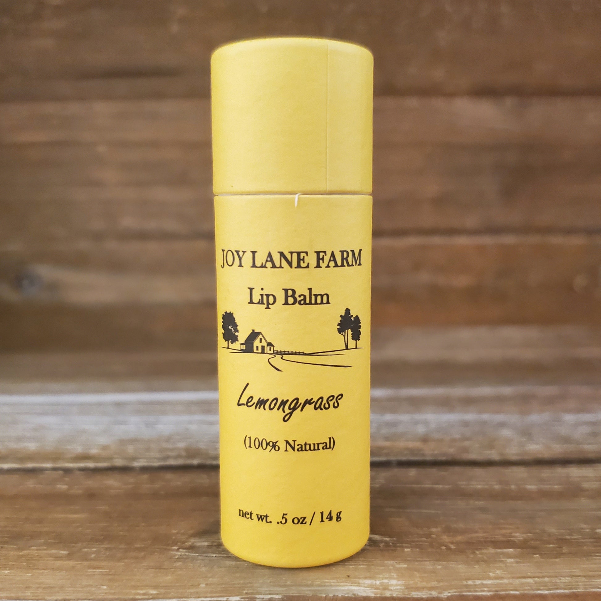 Yellow lip balm container with 'Joy Lane Farm' branding on a wooden background