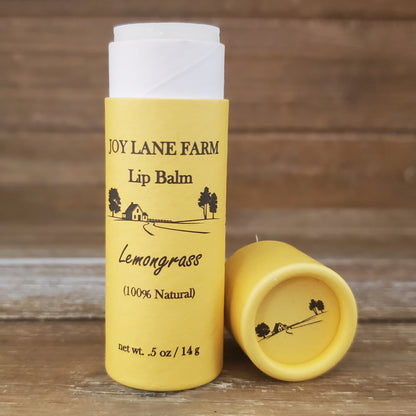 Yellow lip balm with white cap on a wooden surface, featuring 'Joy Lane Farm' branding.