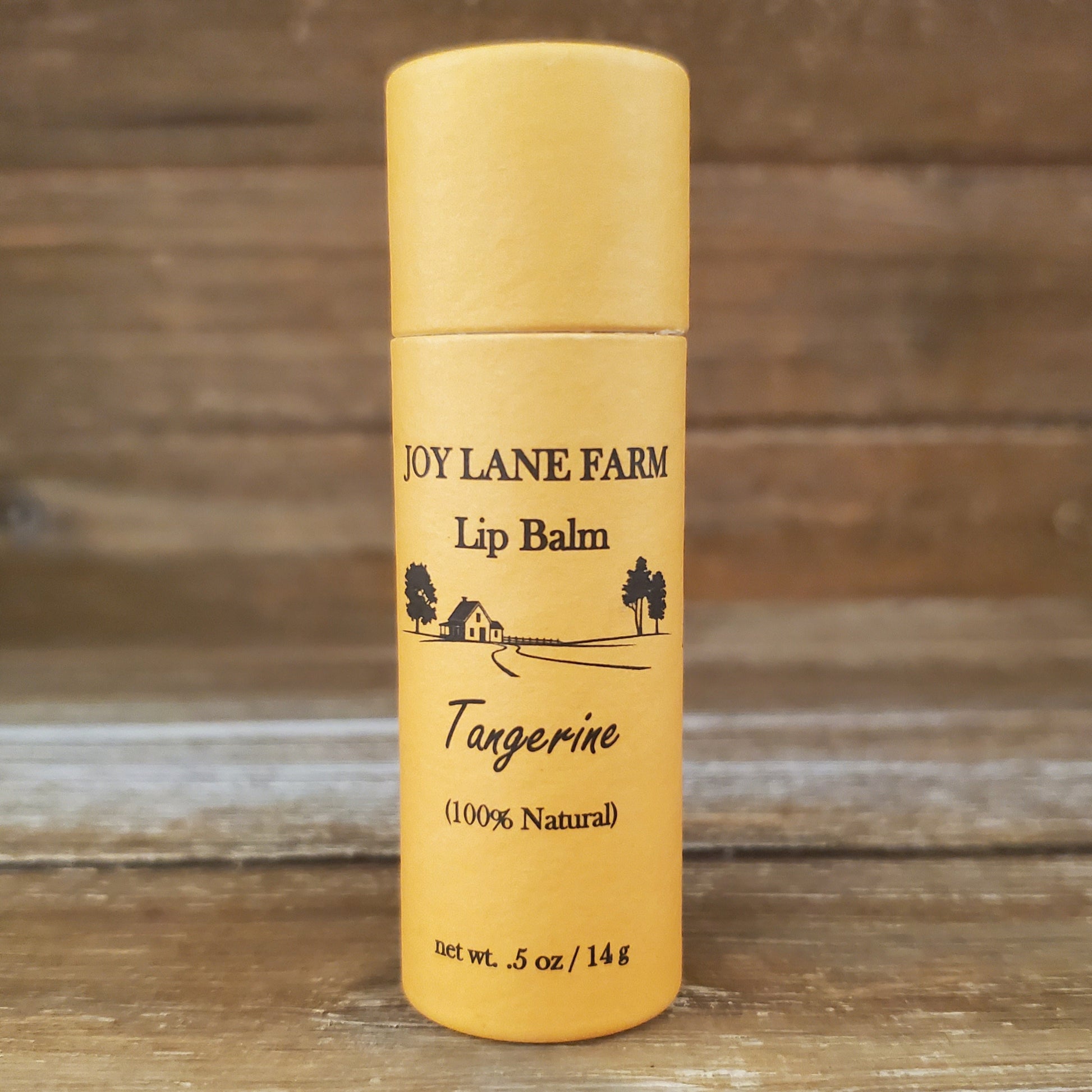 Lip balm container with 'Joy Lane Farm' branding on a wooden background