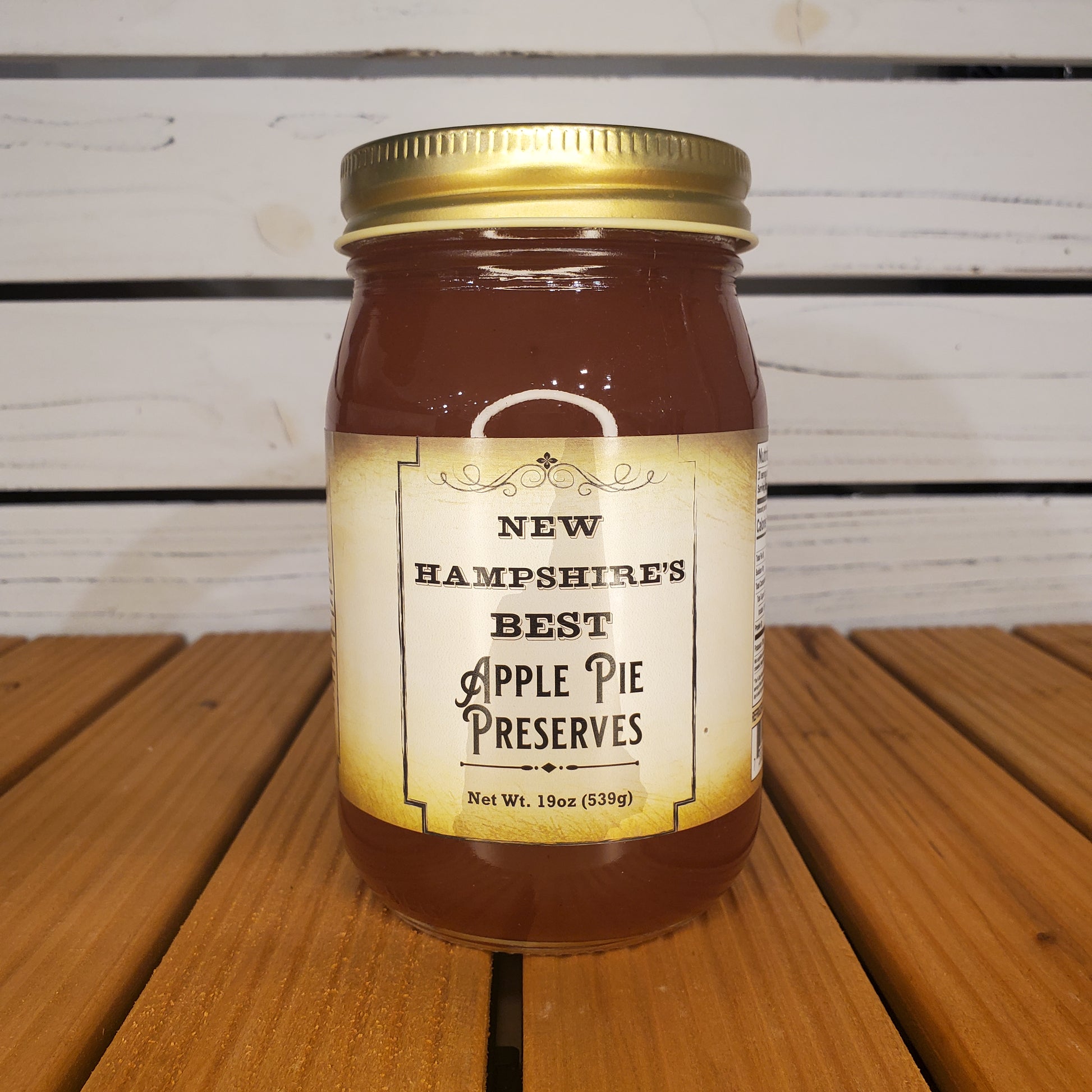 Jar of New Hampshire's Best Apple Pie Preserves on a wooden surface with a white slatted background