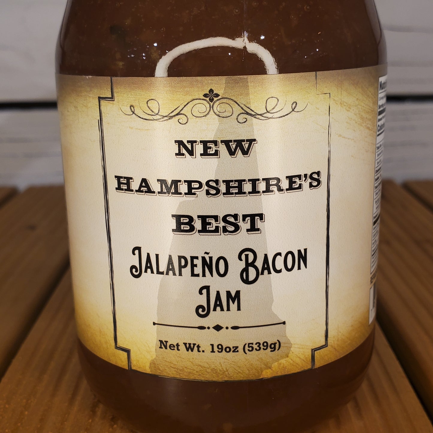 Jar of New Hampshire's Best Jalapeno Bacon Jam with a label on a wooden surface.