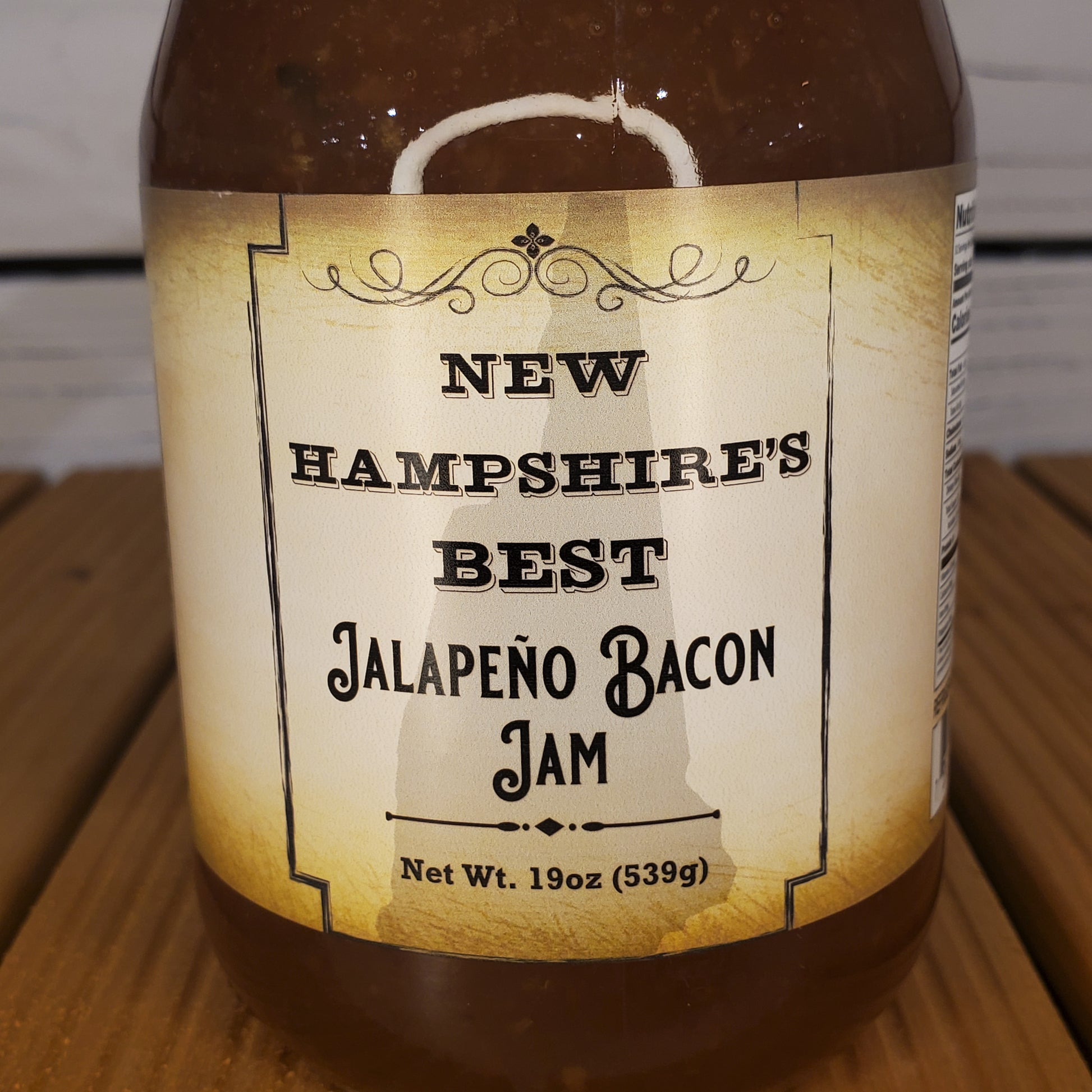Jar of New Hampshire's Best Jalapeno Bacon Jam with a label on a wooden surface.