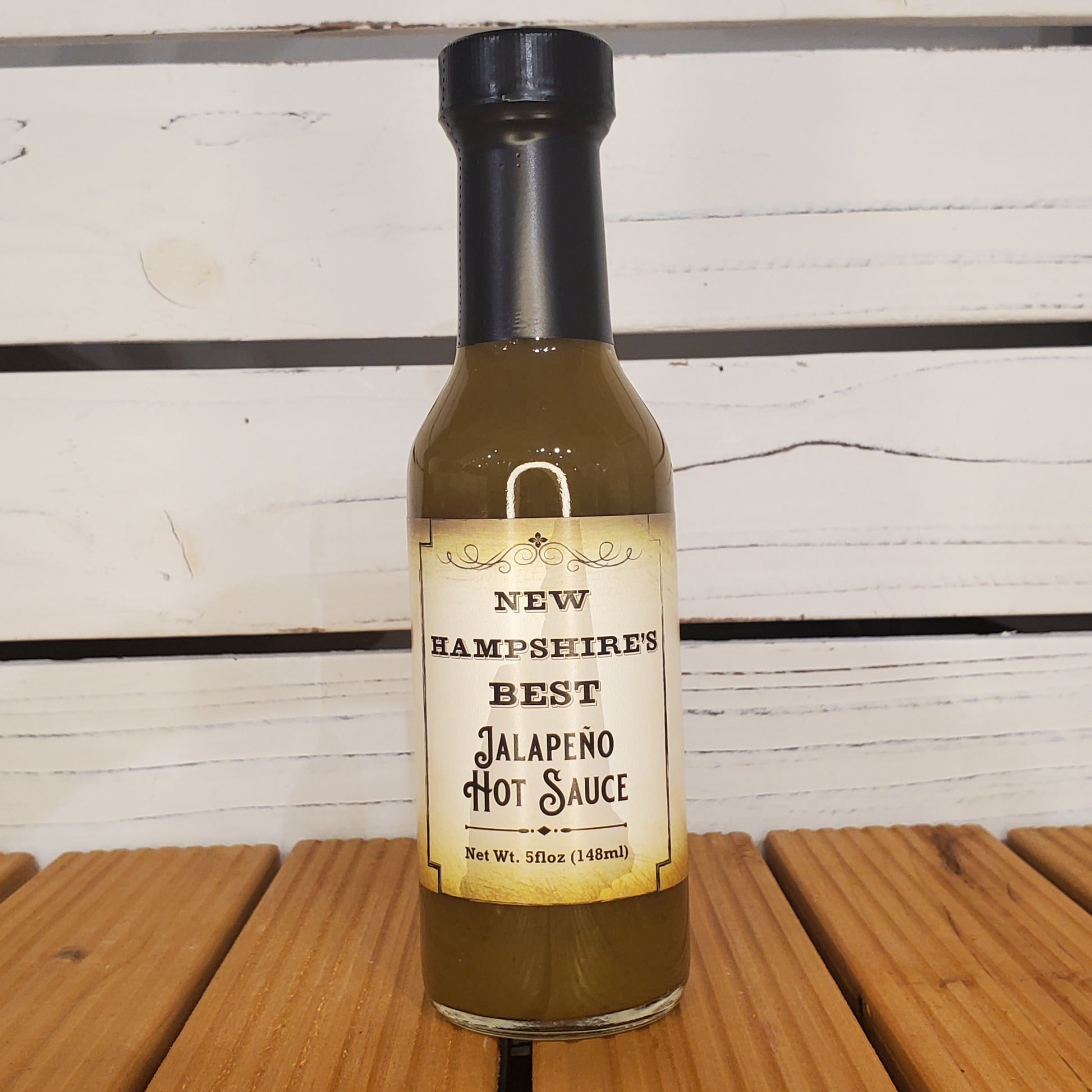 Bottle of New Hampshire Best Jalapeno Hot Sauce on a wooden surface with a white background