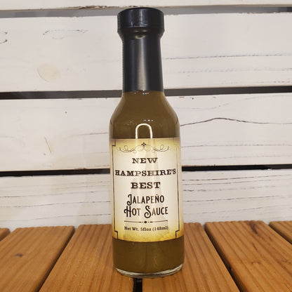 Bottle of New Hampshire Best Jalapeno Hot Sauce on a wooden surface with a white background