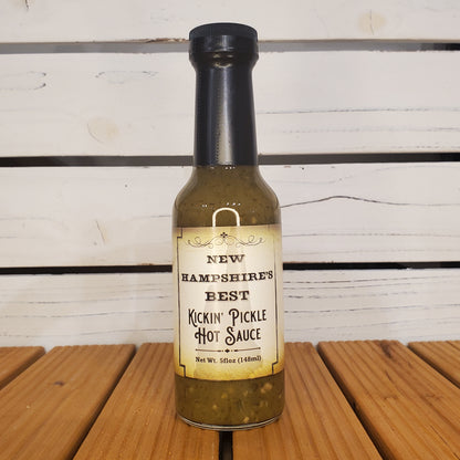 Bottle of New Hampshire's Best Kickin' Pickle Hot Sauce on a wooden surface with a white background
