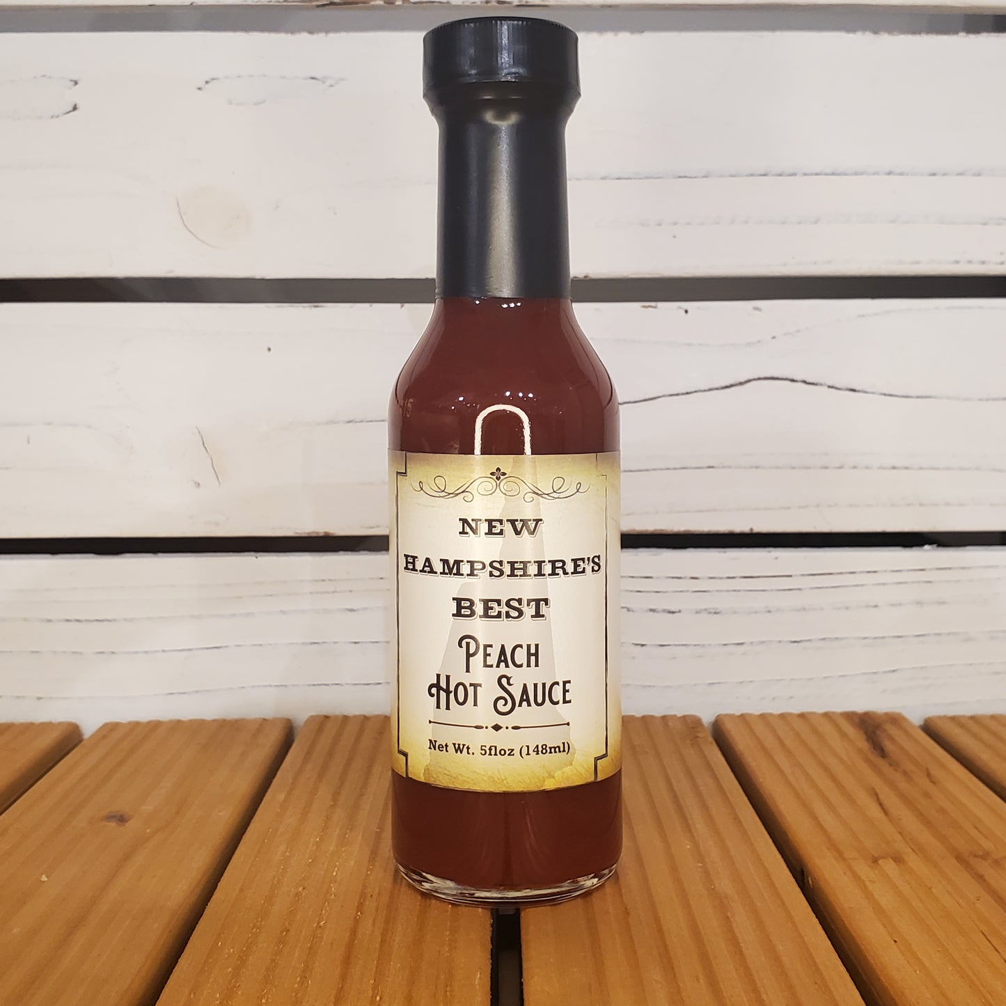 Bottle of New Hampshire's Best Peach Hot Sauce on a wooden surface with a white background