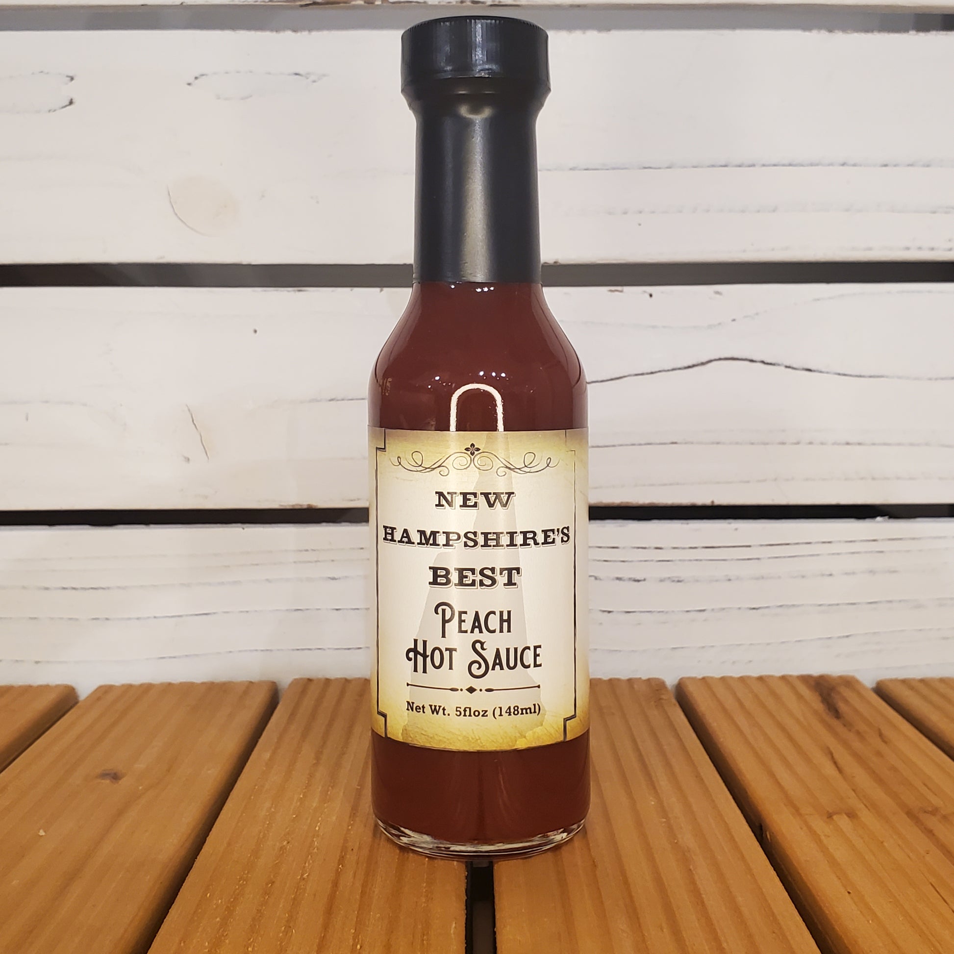 Bottle of New Hampshire's Best Peach Hot Sauce on a wooden surface with a white background