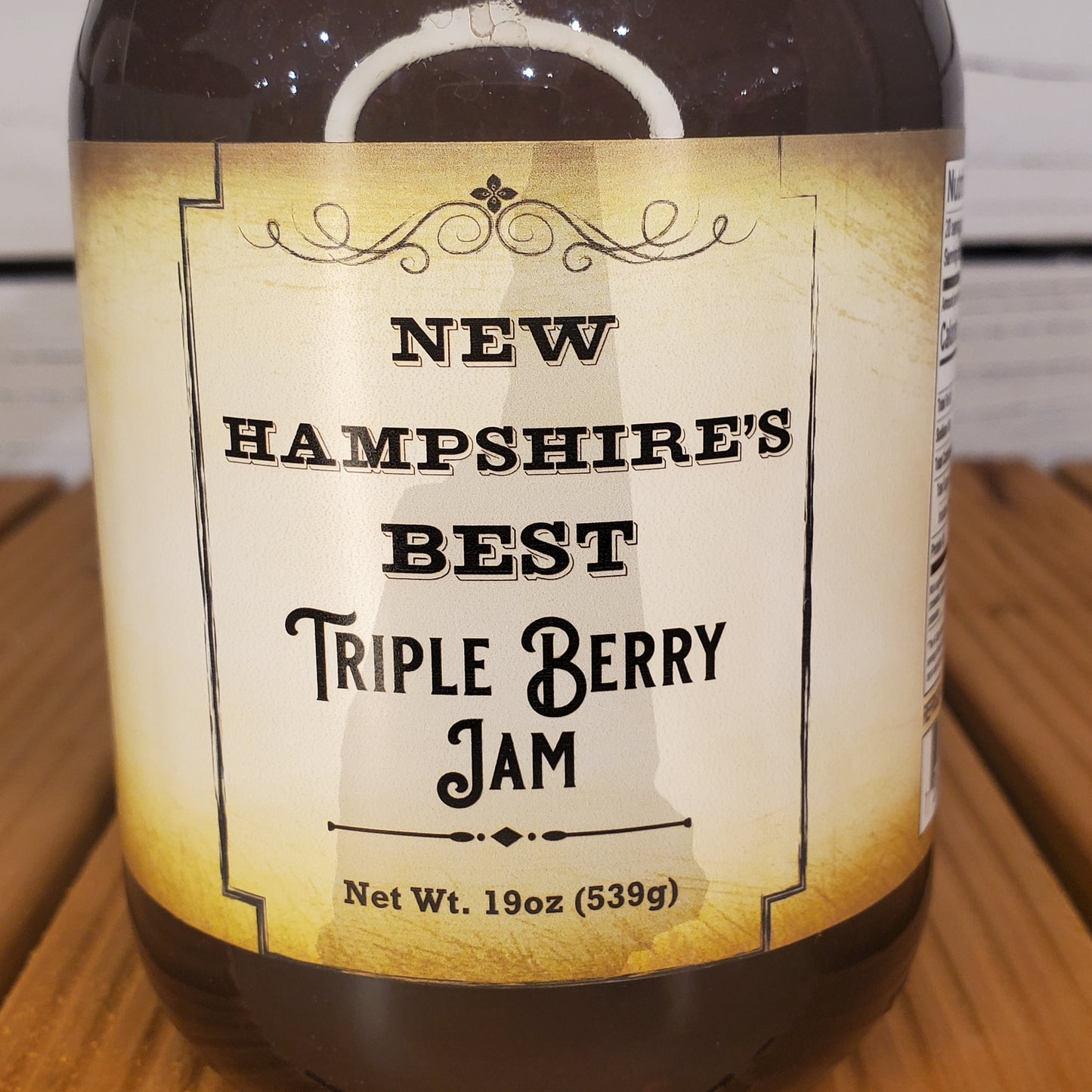 Bottle of New Hampshire's Best Triple Berry Jam with a label on a wooden surface.