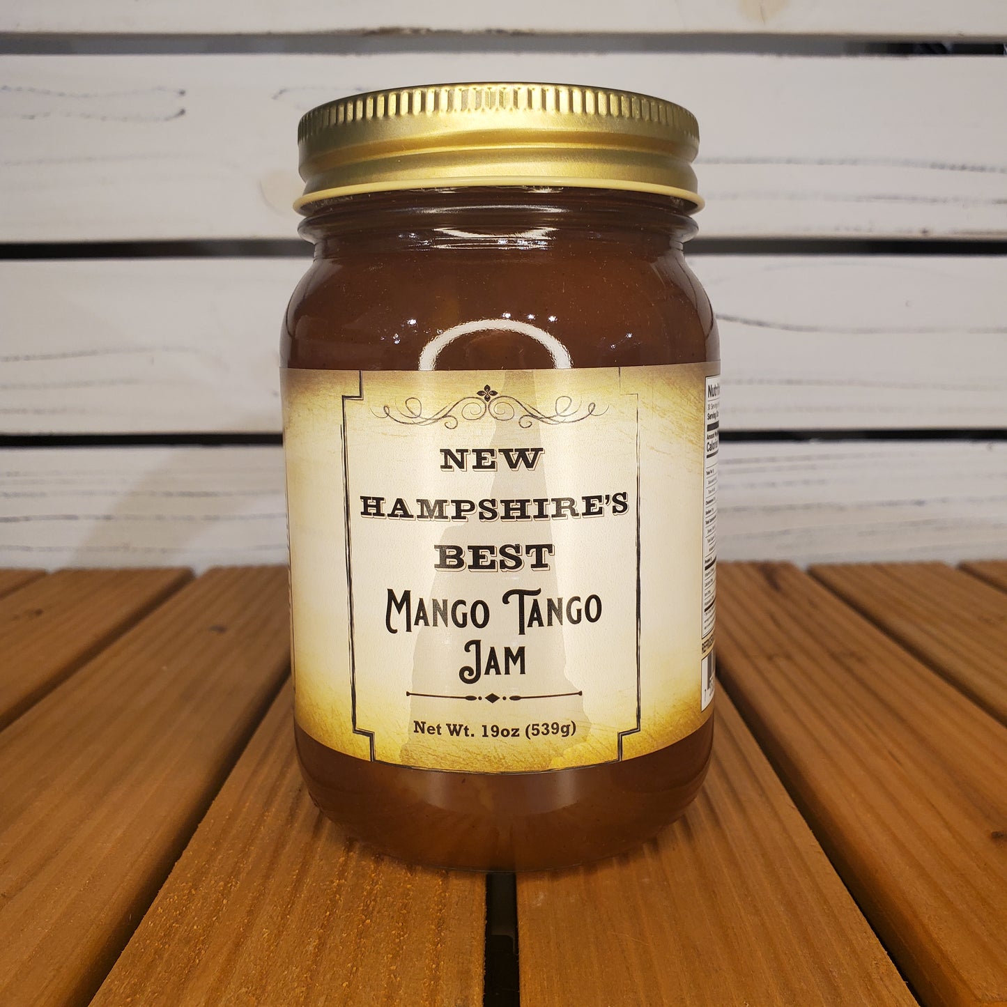 Jar of New Hampshire's Best Mango Tango Jam on a wooden surface with a white slatted background