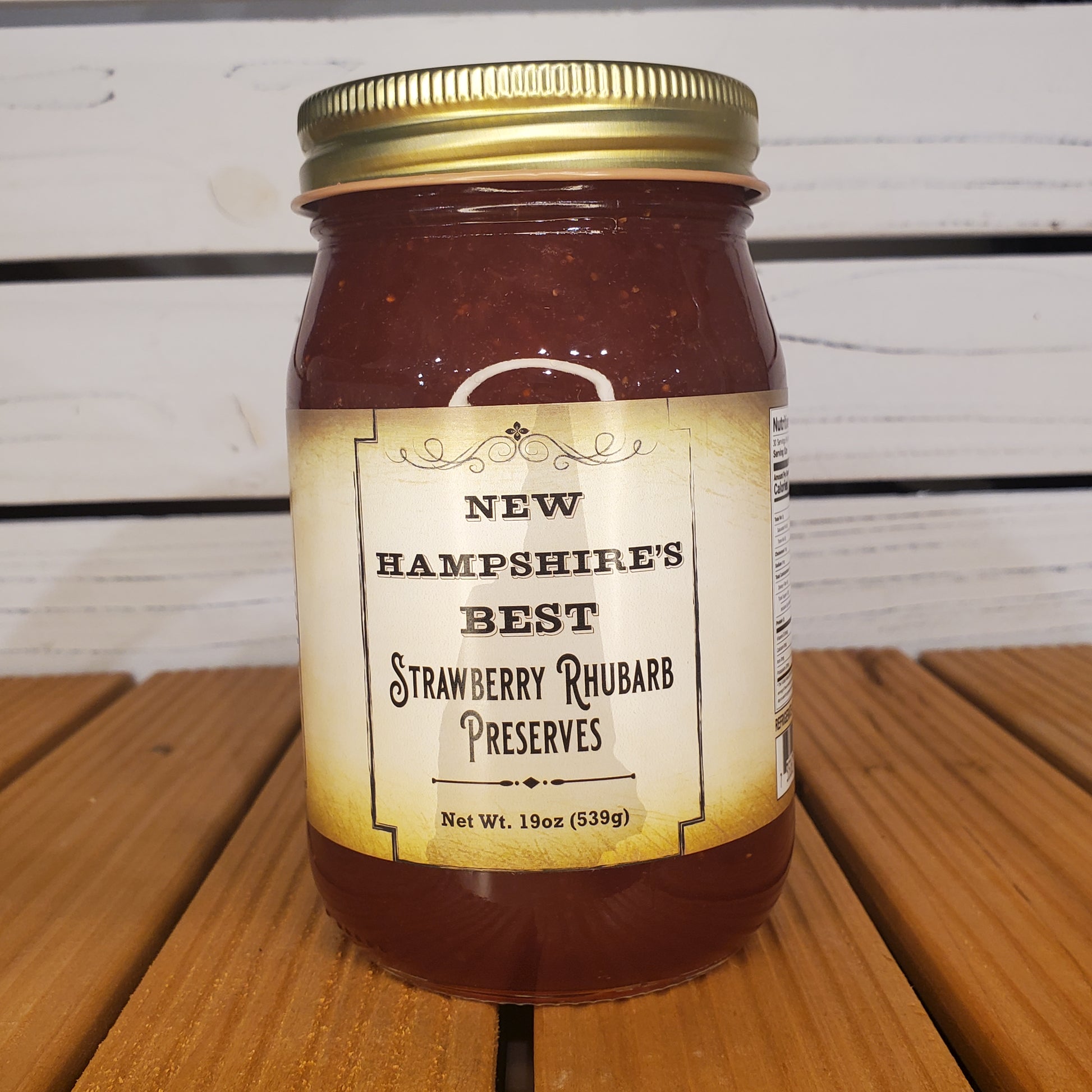 Jar of New Hampshire's Best Strawberry Rhubarb Preserves on a wooden surface with a white background