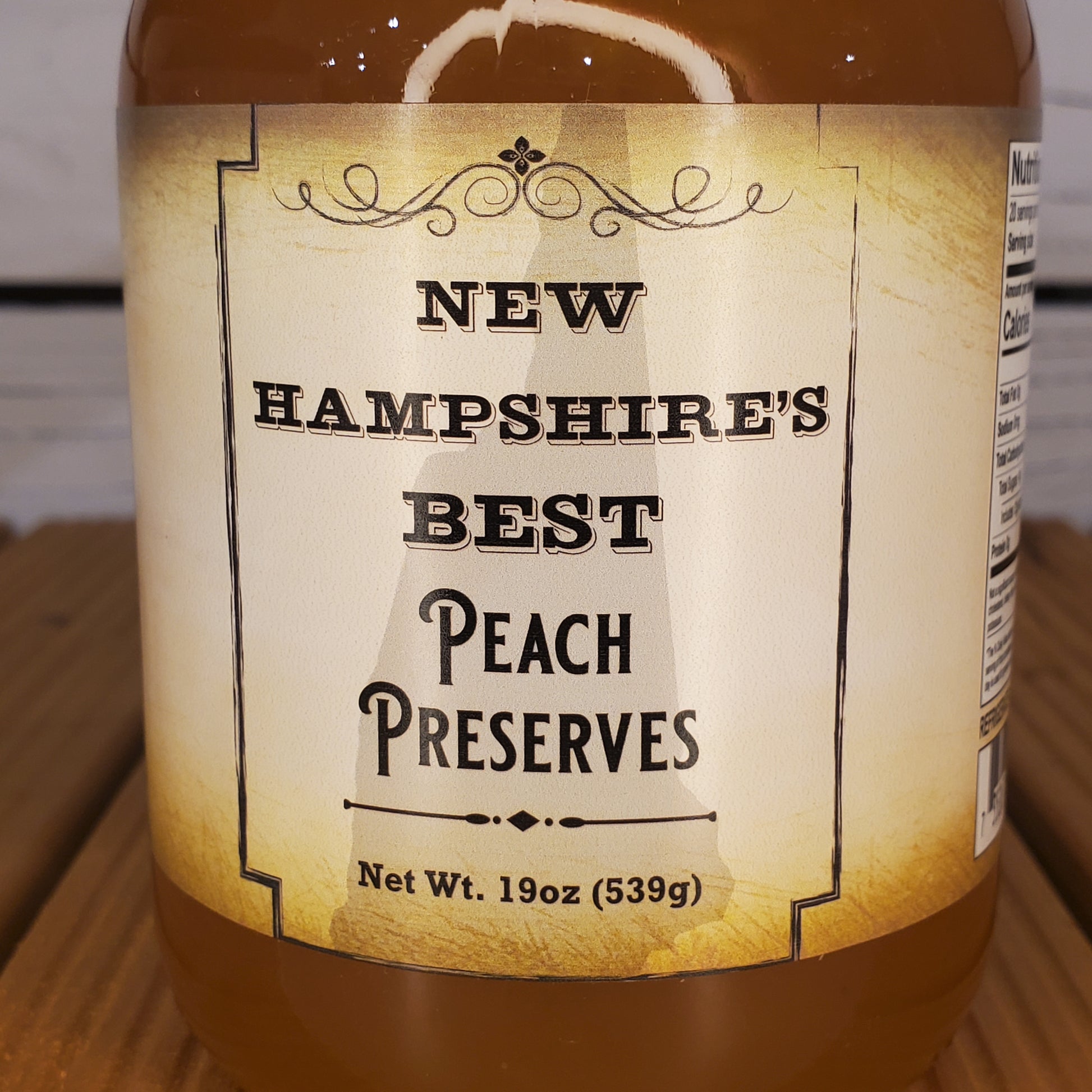 Bottle of New Hampshire's Best Peach Preserves with a label on a wooden surface.