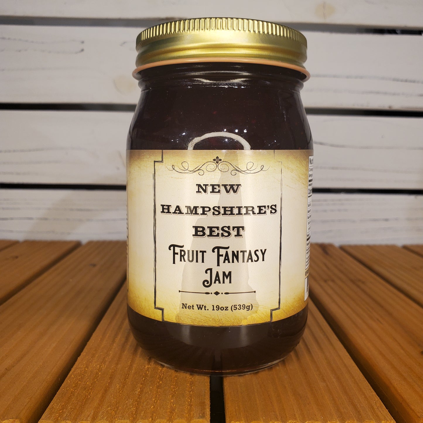 Jar of New Hampshire's Best Fantasy Fruit Jam with a gold lid on a wooden surface.