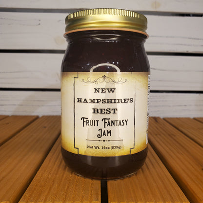Jar of New Hampshire's Best Fantasy Fruit Jam with a gold lid on a wooden surface.