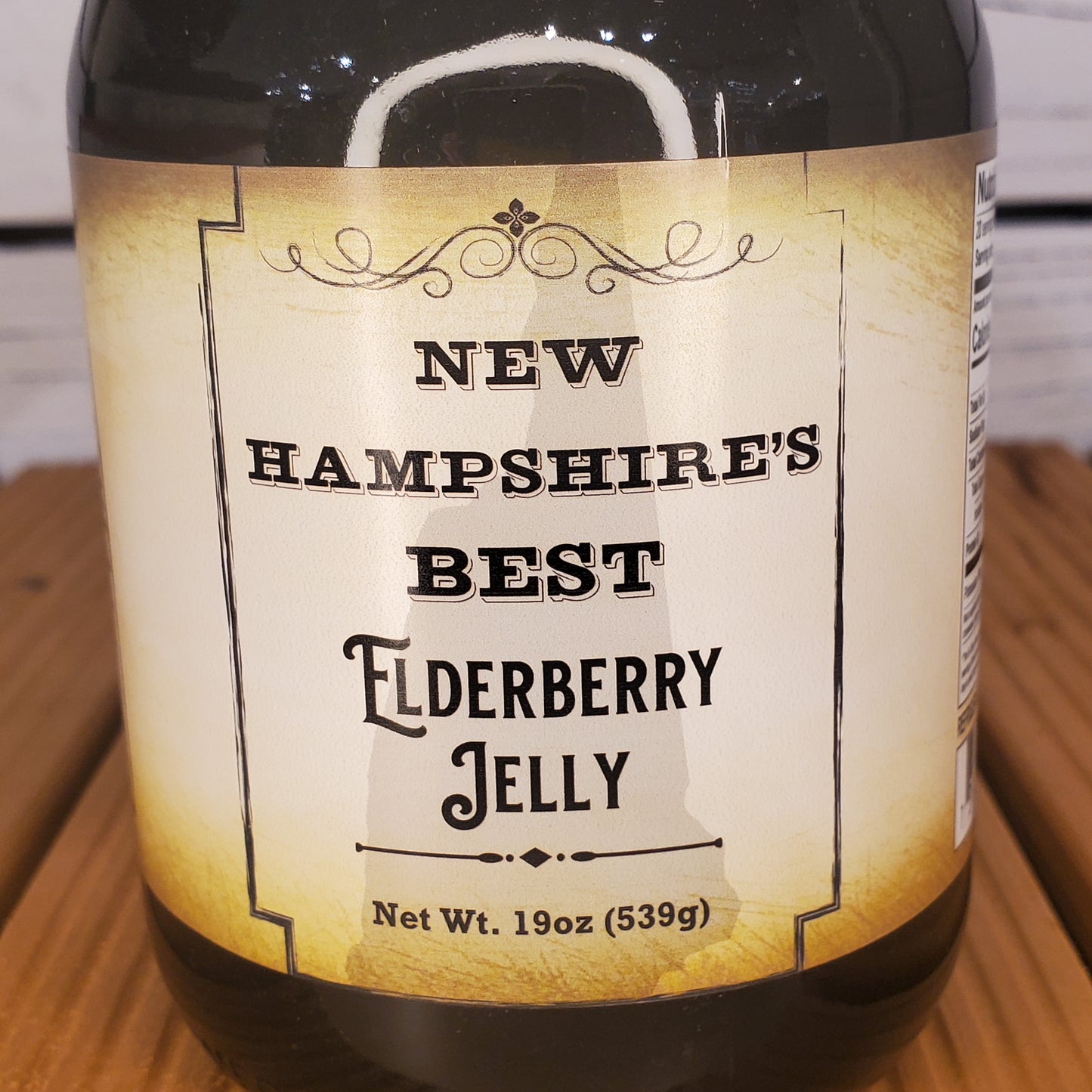 Bottle of New Hampshire's Best Elderberry Jelly with a label on a wooden surface.
