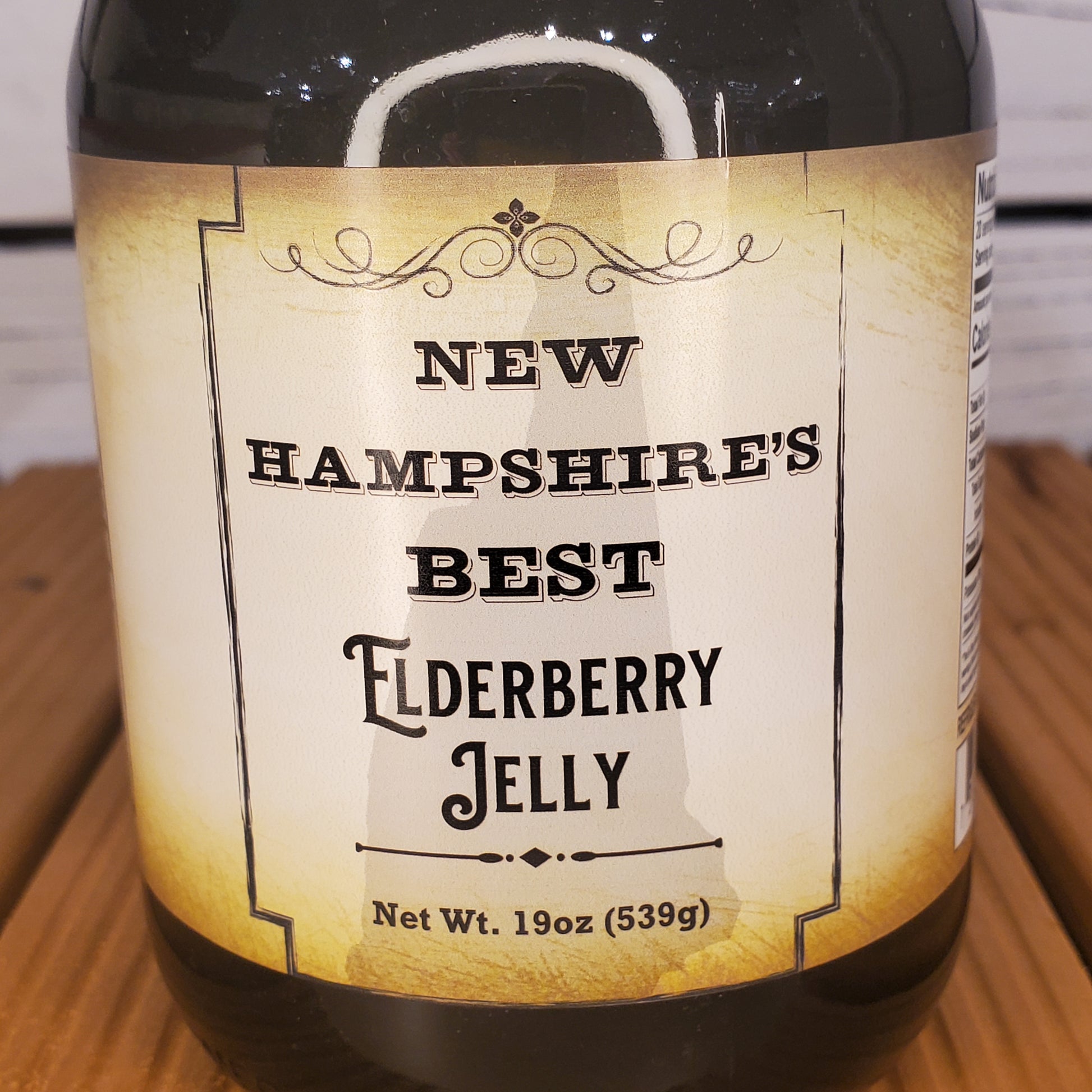Bottle of New Hampshire's Best Elderberry Jelly with a label on a wooden surface.