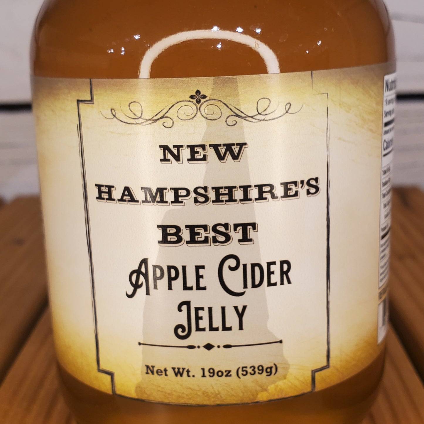 Bottle of New Hampshire's Best Apple Cider Jelly with a label on a wooden surface.