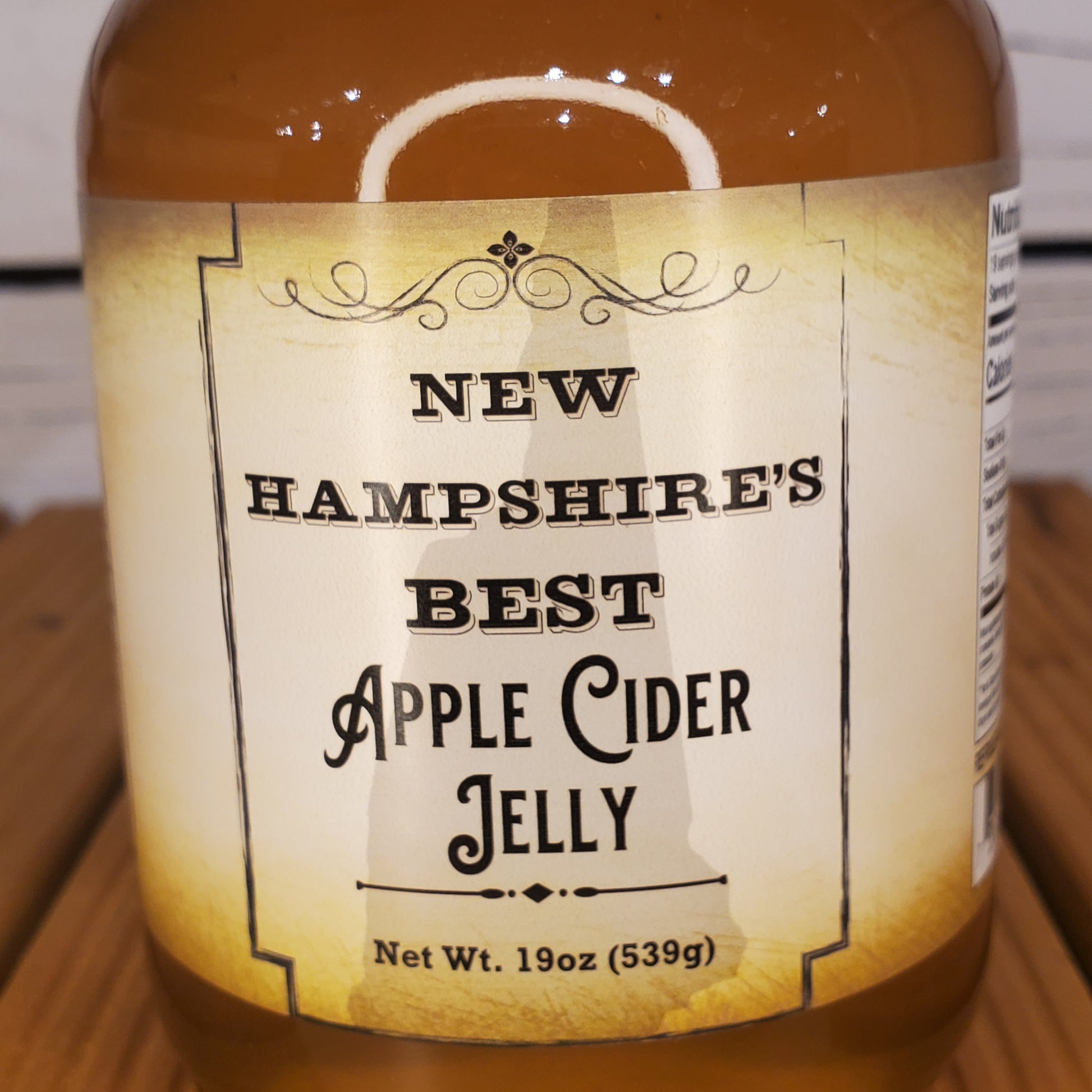 Bottle of New Hampshire's Best Apple Cider Jelly with a label on a wooden surface.