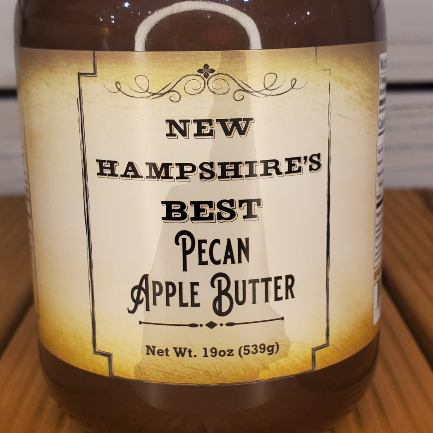 Jar of New Hampshire's Best Pecan Apple Butter with a label on a wooden surface.