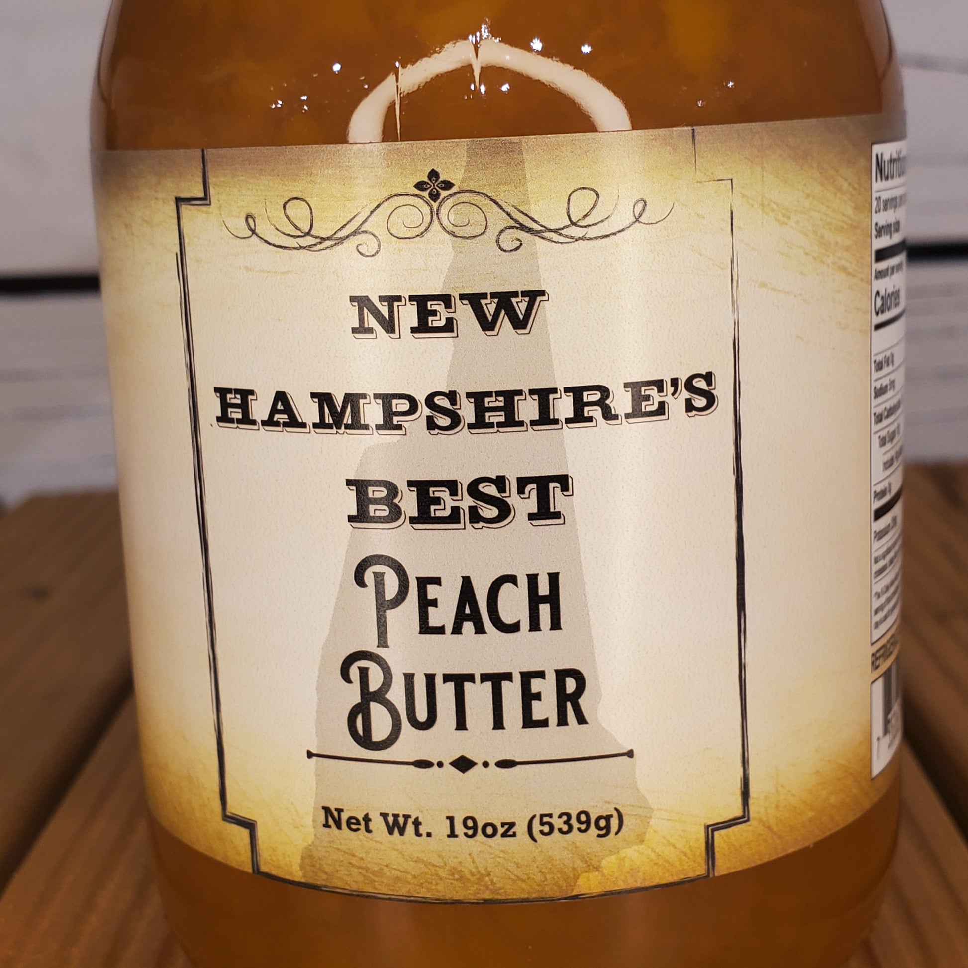 Jar of New Hampshire's Best Peach Butter with a label on a wooden surface.