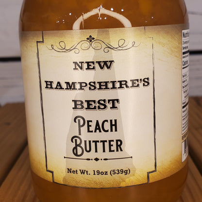 Jar of New Hampshire's Best Peach Butter with a label on a wooden surface.