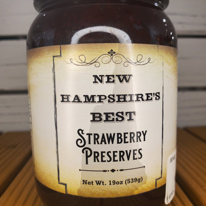 Jar of New Hampshire's Best Strawberry Preserves with a label on a wooden surface.