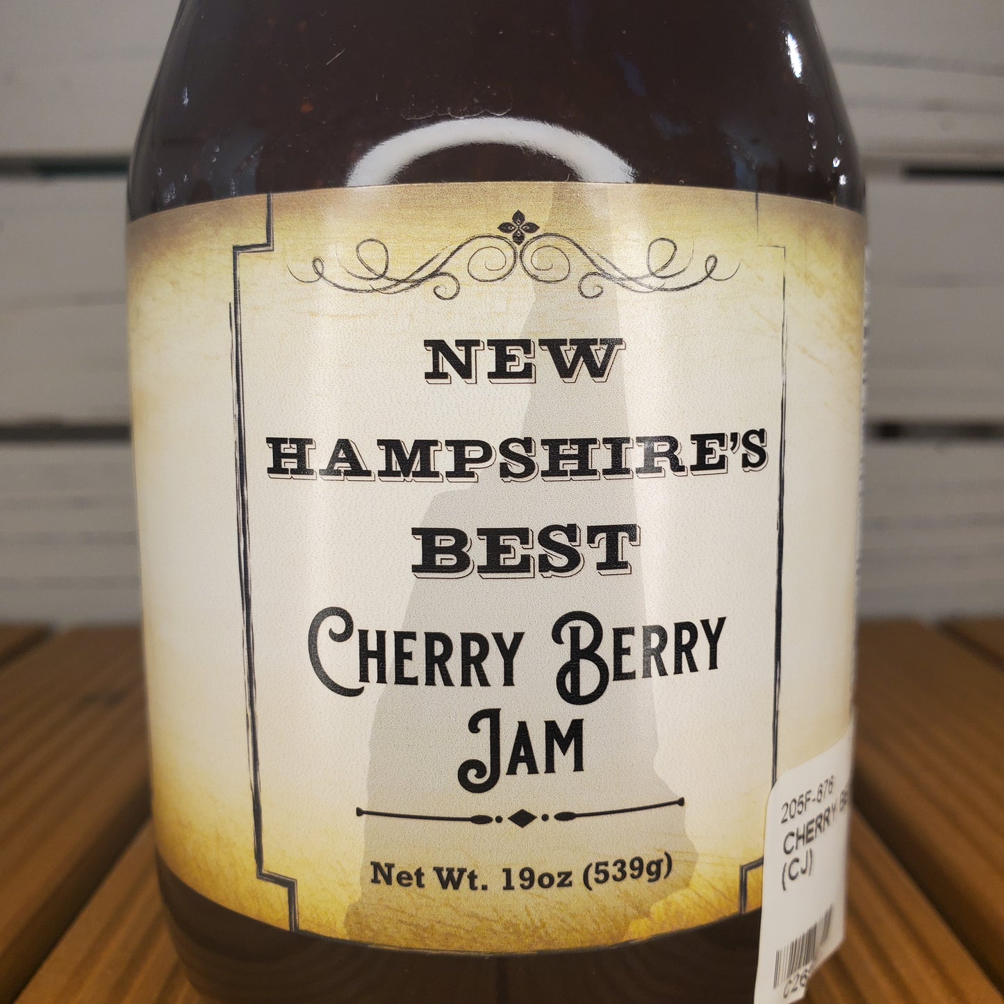 Jar of New Hampshire's Best Cherry Berry Jam with a label on a wooden surface.