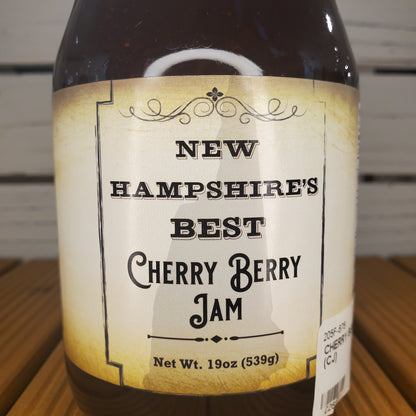 Jar of New Hampshire's Best Cherry Berry Jam with a label on a wooden surface.