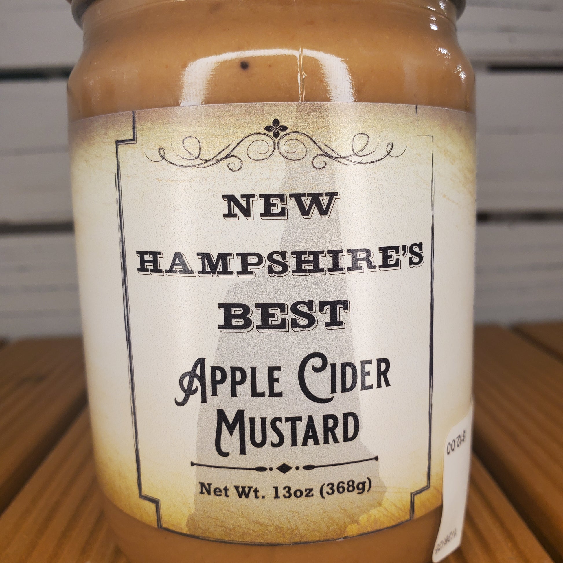 Bottle of New Hampshire's Best Apple Cider Mustard with a label on a wooden surface.