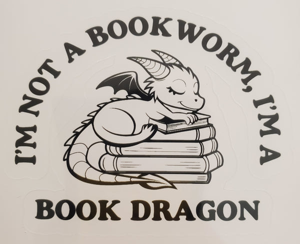 A black and white graphic sticker or decal featuring a cute cartoon book dragon curled up inside stacked books, with the text 'I'M NOT A BOOK WORM, I'M A BOOK DRAGON' around it.