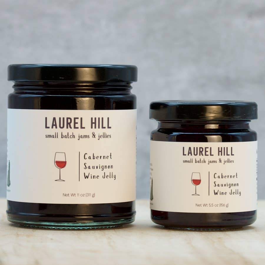 Two jars of Laurel Hill Cabernet Sauvignon Wine Jelly on a marble surface with a gray background.