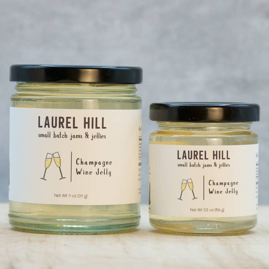 Two glass jars of Laurel Hill Small Batch Jams & Jellies, one larger and one smaller, both filled with Champagne Wine Jelly and topped with black lids, set on a light marble surface against a neutral gray background.