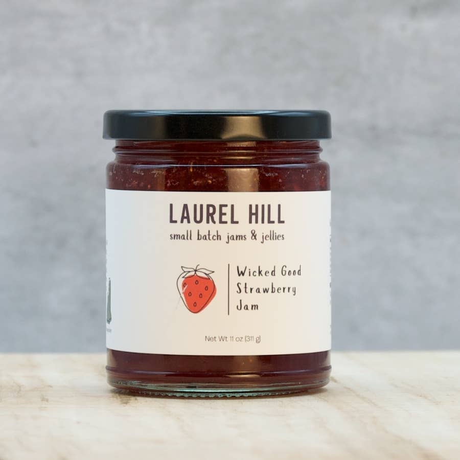 Jar of Laurel Hill Wicked Good Strawberry Jam on a wooden surface with a gray background