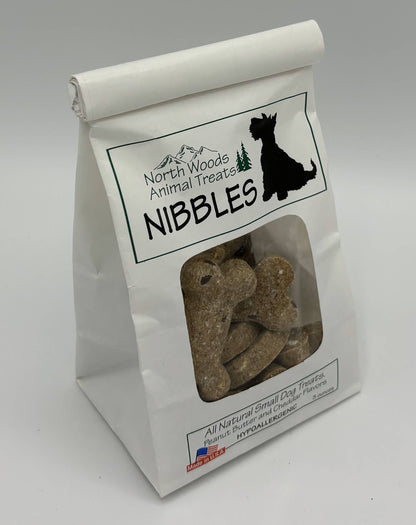A white stand-up paper bag of North Woods Animal Treats Nibbles dog treats, featuring a clear window that displays the brown bone-shaped treats inside.