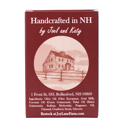 A rectangular product box for Handcrafted in NH by Joel and Katy, featuring a dark red background with white text and a circular illustration of a farmhouse. The box includes ingredient details and the website Restock at JoyLaneFarm.