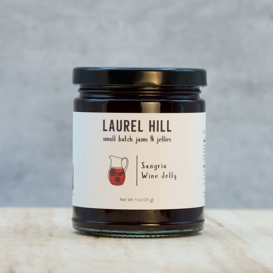 A glass jar of Laurel Hill Small Batch Jams & Jellies, Sangria Wine Jelly, with a black lid and white label, set on a light marble surface against a textured gray background.