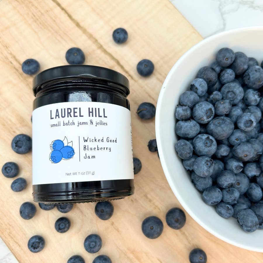 Jar of Laurel Hill Wicked Good Blueberry Jam with blueberries on a wooden surface