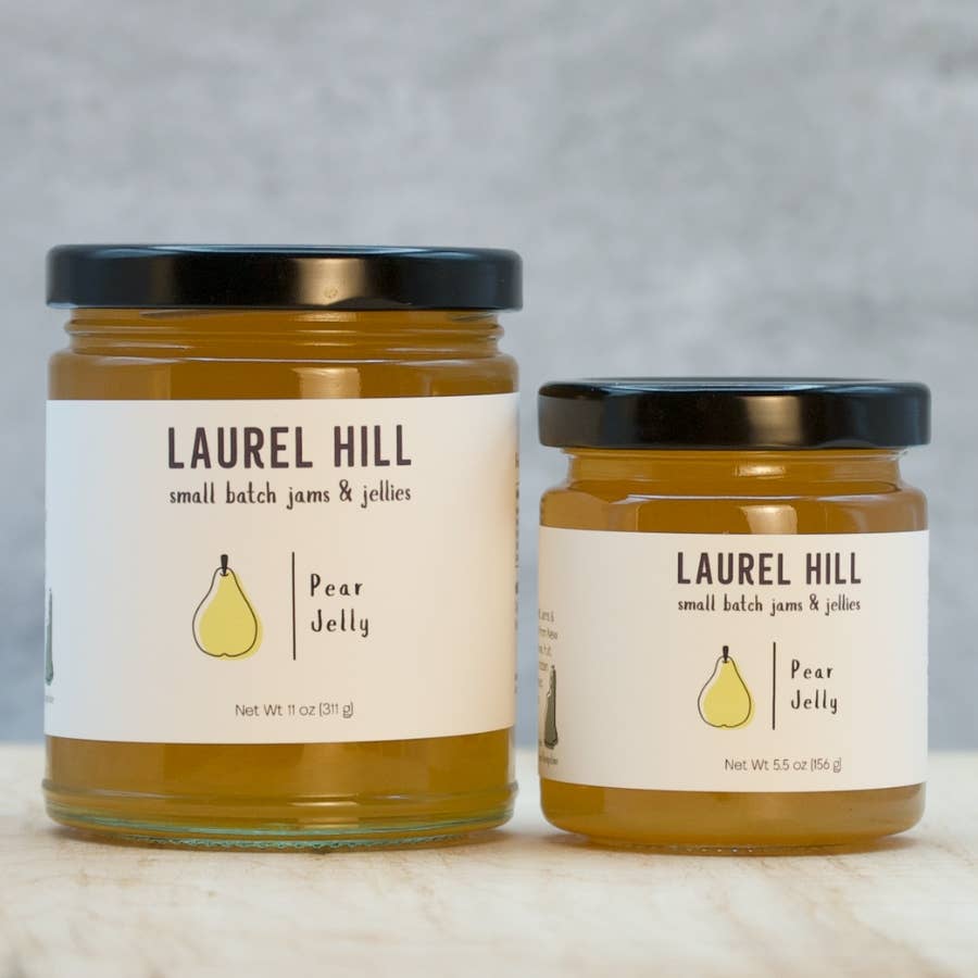 Two glass jars of Laurel Hill Pear Jelly with black lids and cream labels, displayed on a light marble surface against a gray textured background.
