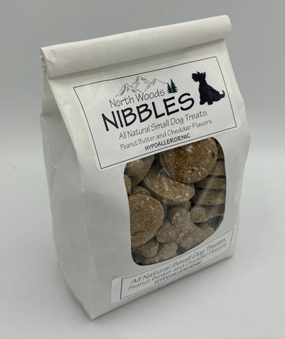 A white stand-up bag of North Woods Nibbles dog treats with a clear window showing round brown treats inside, photographed on a light gray background.