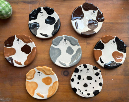 Set of ceramic dog plates with different color patterns on a wooden surface.