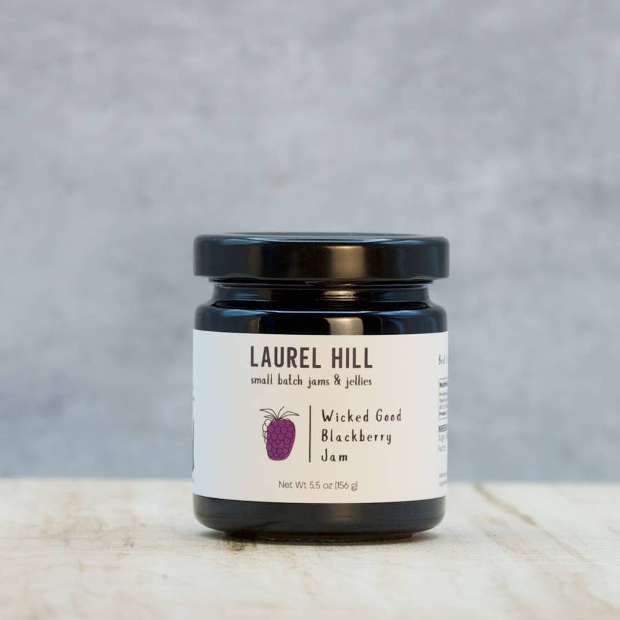 Jar of Laurel Hill Wicked Good Blackberry Jam on a wooden surface with a gray background