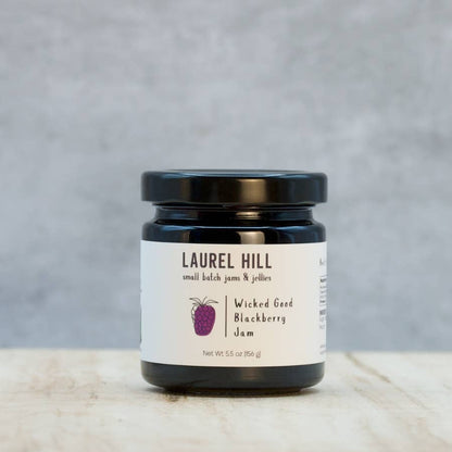 Jar of Laurel Hill Wicked Good Blackberry Jam on a wooden surface with a gray background