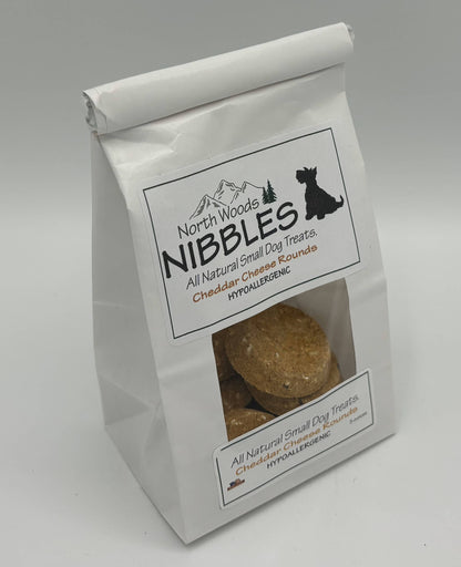 A white stand-up bag of North Woods Nibbles cheddar cheese round dog treats, featuring a clear window on the lower front showing the round treats inside.