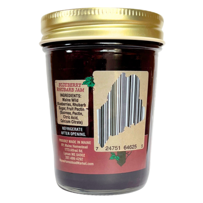 A glass jar of Blueberry Rhubarb Jam with a gold metal lid, showing the back label with a barcode and product details on a white background.