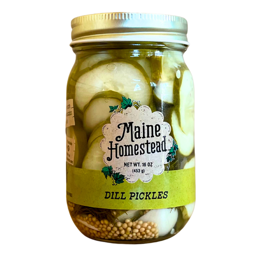 A glass jar of Maine Homestead Dill Pickles with a gold metal lid and a white and green label, containing sliced dill pickles and mustard seeds, isolated on a white background.