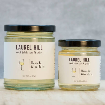 Two glass jars of Laurel Hill Small Batch Jams & Jellies, one larger 11 oz jar and one smaller 5.5 oz jar, both filled with pale yellow jelly and topped with black lids, set on a light marble surface against a textured gray background.