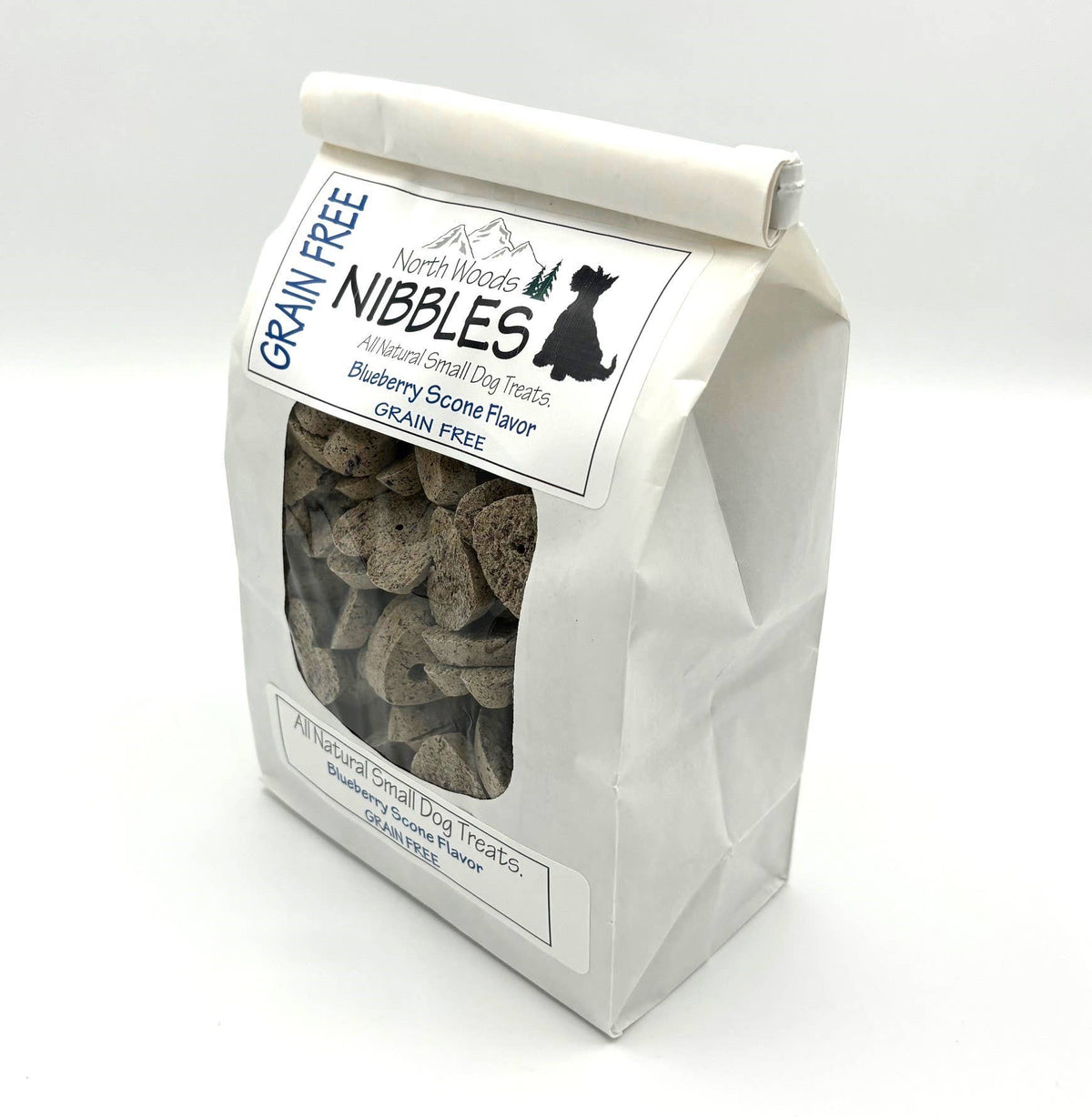A white stand-up paper bag of North Woods Nibbles grain-free small dog treats, shown on a clean white background. The bag has a clear front window displaying the brownish treats inside, with a white label featuring blue and black text.