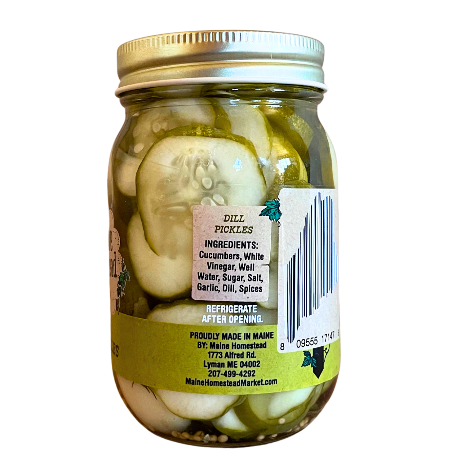 A glass jar of Maine Homestead Dill Pickles filled with sliced cucumbers in brine, topped with a gold metal lid, and featuring a white and green label with a barcode.