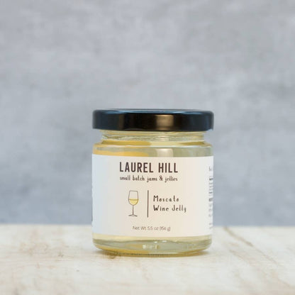 A jar of Laurel Hill Moscato Wine Jelly with a black lid and white label, set on a light marble surface against a textured gray background.
