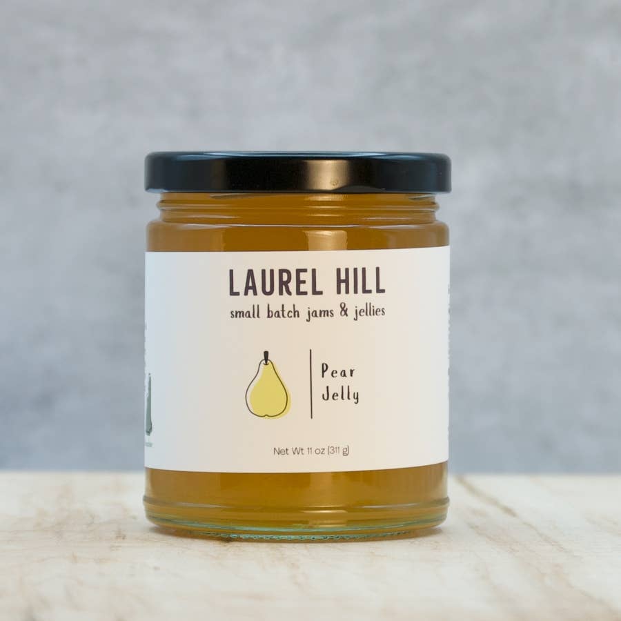 A glass jar of Laurel Hill Pear Jelly with a black lid and a white label, set on a light wooden surface against a textured gray background.
